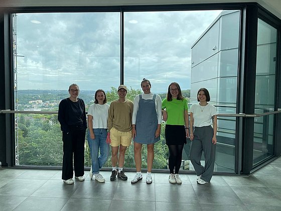 Nebeneinander von links nach rechts: Tina Nobis, Lara Kronenbitter, Mahima Rai, Annika Schwark, Sophia Aalders, Franziska Storm vor großem Glasfenster in BUW-Räumen